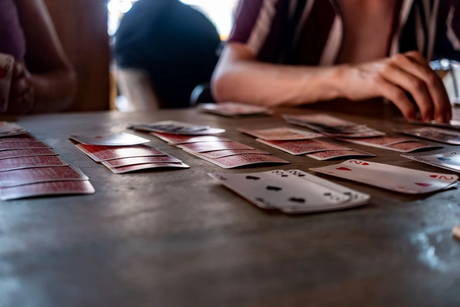 Des cartes étalées sur une table en bois pendant une partie, plusieurs mains de joueurs autour