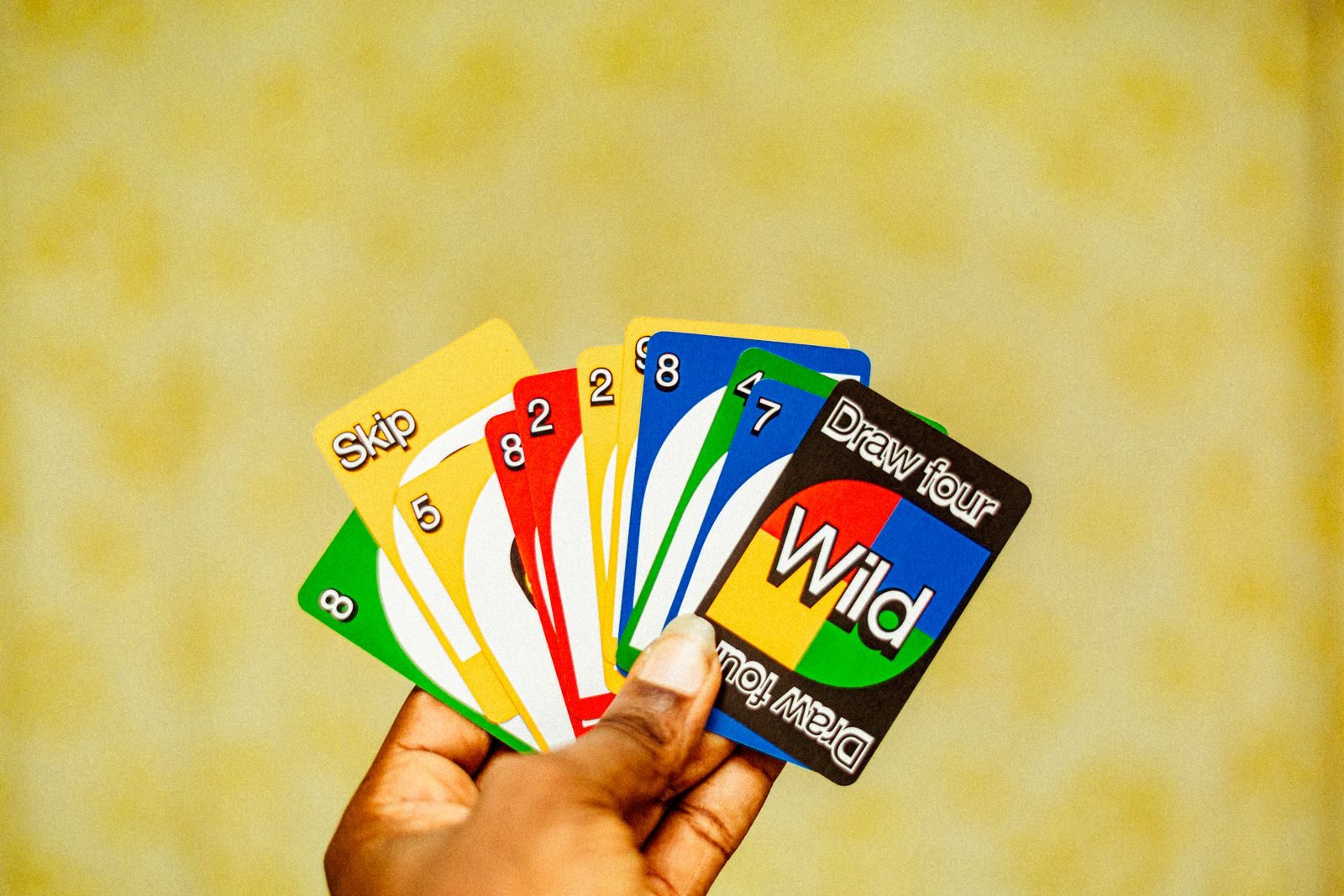 Une main tient des cartes Uno dont une carte Passer, une carte Joker et une carte Draw Four aux couleurs vives
