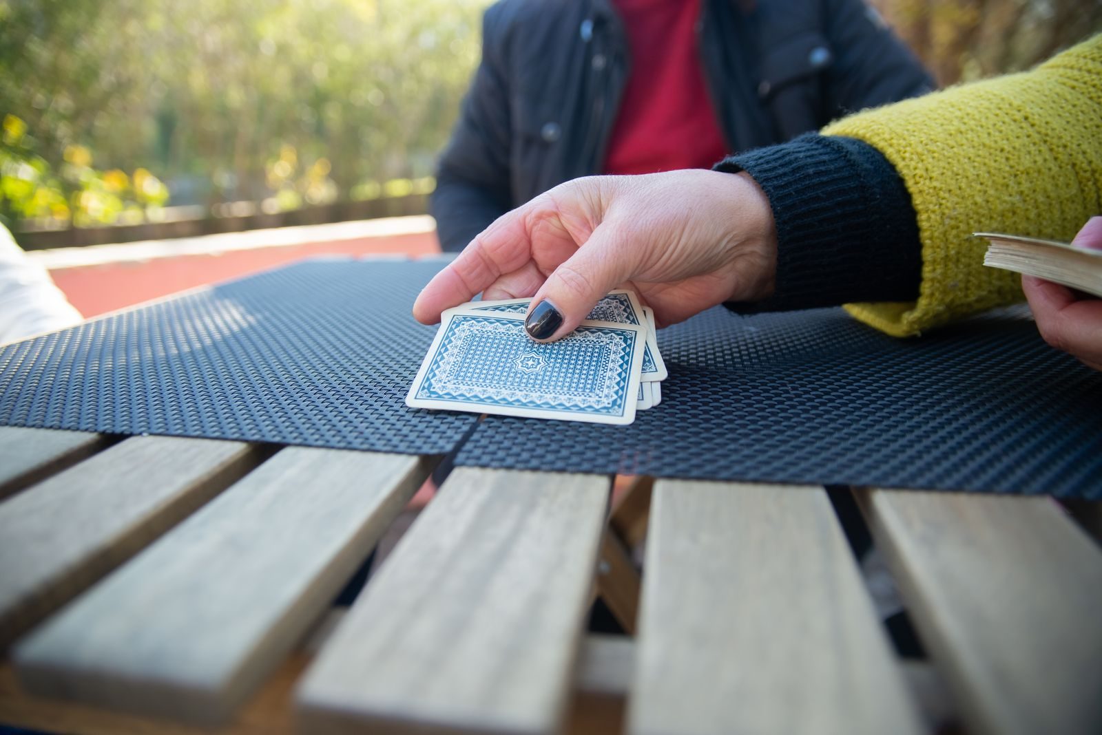 Une main pose des cartes faces cachées sur une table de jardin au cours d'une partie