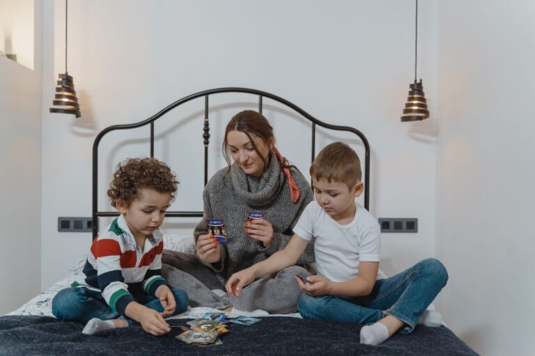 Une mère et deux enfants jouent aux cartes assis sur un lit
