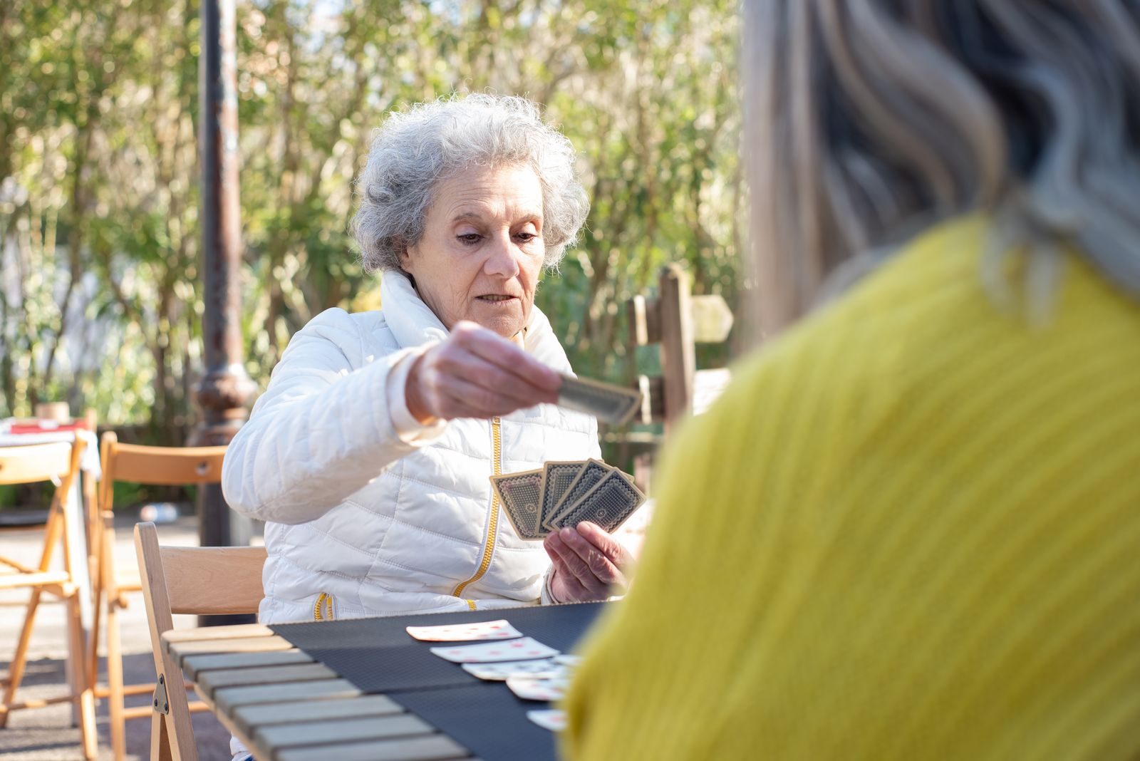 Une femme âgée joue aux cartes à une table en plein air